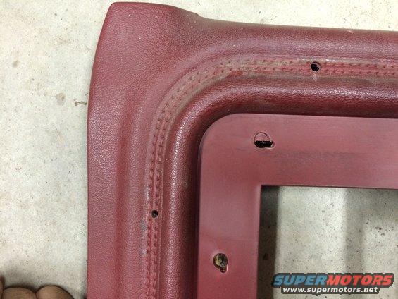 Close-up of a red vinyl interior trim piece with stitched detailing and screw holes