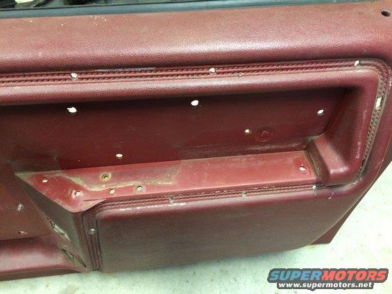 Maroon car door panel with visible screw holes and textured handle area