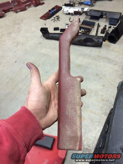 Hand holding a red interior trim piece with dust. Other disassembled car parts are on the floor