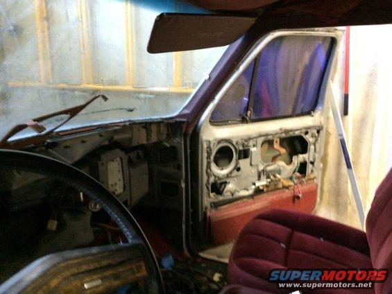 Disassembled vehicle interior with door panel removed, showing exposed metal and wiring. Maroon seat visible