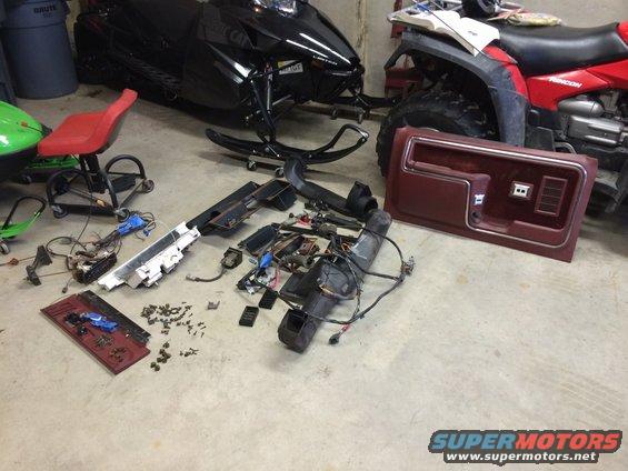 Disassembled vehicle interior parts including a door panel, dashboard components, and wiring harnesses spread on a concrete floor