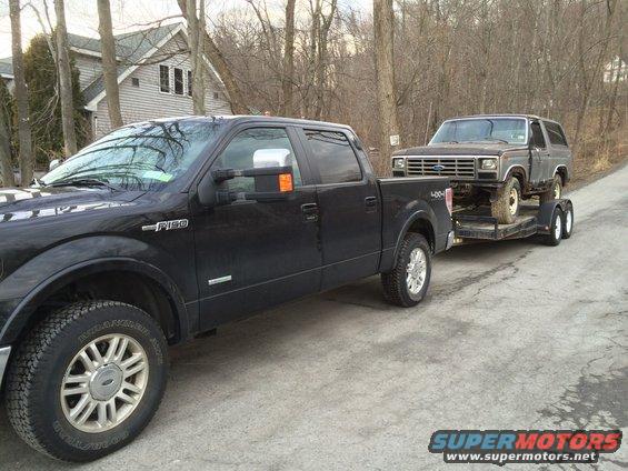 Gray 1980s Ford Bronco on trailer, towed by black F-150
