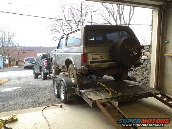 Ford Bronco being towed on a trailer behind a pickup truck, with an SUV visible in the background