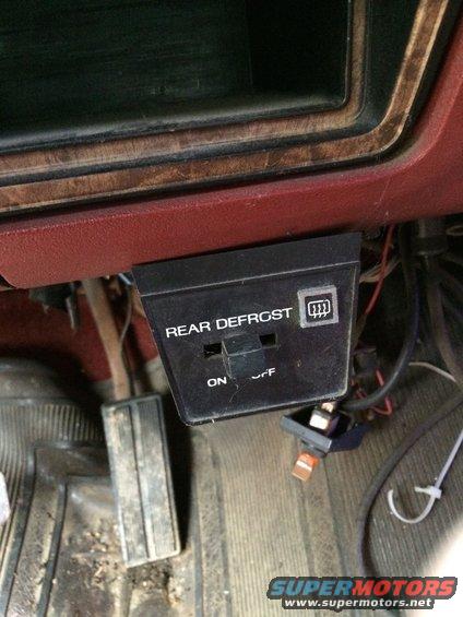 Interior view of a vehicle's dashboard showing a rear defrost switch and pedals