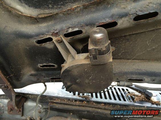 under hood component with a silver dome and black housing, mounted to rusty metal