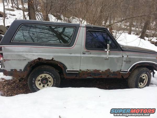 1986 Ford Bronco with significant rust on lower body panels, parked in snow