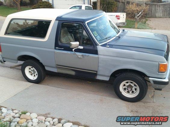 Ford Bronco with primer gray body panels and a white roof, parked on a driveway