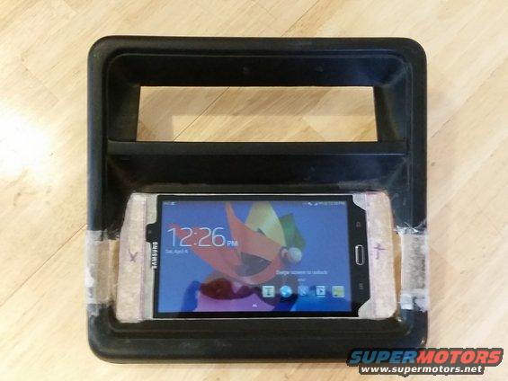 Black plastic dashboard trim piece holding a Samsung smartphone displaying 12:26 PM