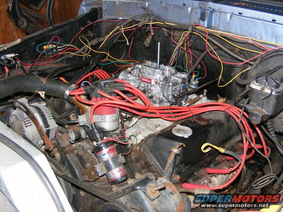 Engine bay with a red-wired distributor, silver carburetor, and tangled wires