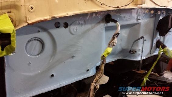 firewall area of a vehicle, painted light blue, with wiring harness taped up