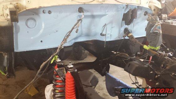Vehicle firewall and frame with suspension components visible, undergoing restoration