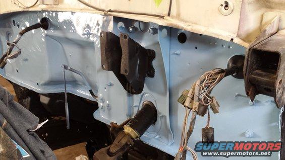 firewall area of a vehicle, painted light blue, with wiring harnesses and mounting brackets