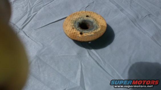 Used oil filter with a central hole and two mounting holes, resting on a grey cloth