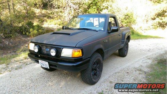 Matte black Ford Ranger pickup truck with aftermarket hood scoop and fog lights. License plate reads 7Y86323