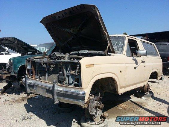 Tan SUV with hood open, missing wheels, in a junkyard