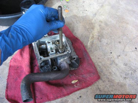 Gloved hand working on carburetor part with metal pipe