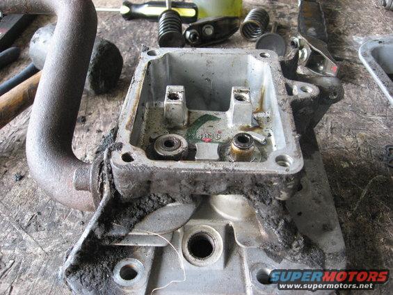 Disassembled engine cylinder head with exhaust pipe attached. Tools and engine parts are visible on the workbench