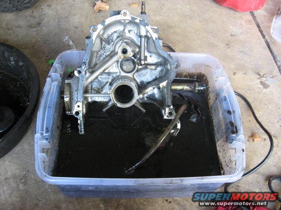 engine block soaking in dark fluid inside a clear plastic tub