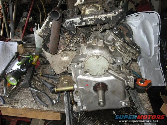 Engine on workbench with tools, tape measure, and parts scattered around