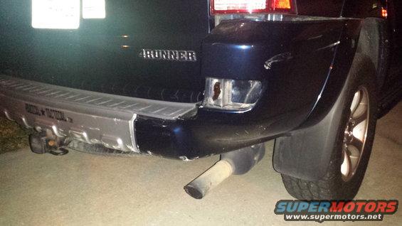 Dark blue SUV rear bumper with visible damage, broken taillight, and exhaust pipe. The word "4RUNNER" is visible