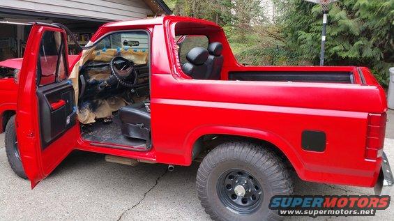 Red Ford Bronco with doors open, interior masked for painting. Seats visible in rear