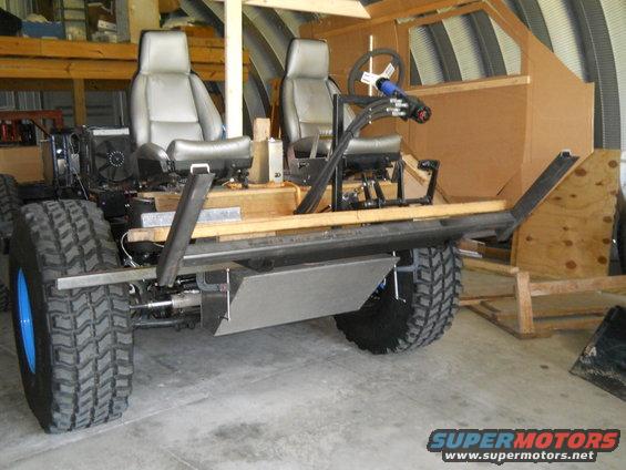 Custom off-road vehicle chassis with two seats, steering wheel, and large tires, in a workshop