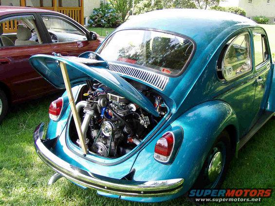 Teal Volkswagen Beetle rear view, engine exposed. Another car is parked next to it
