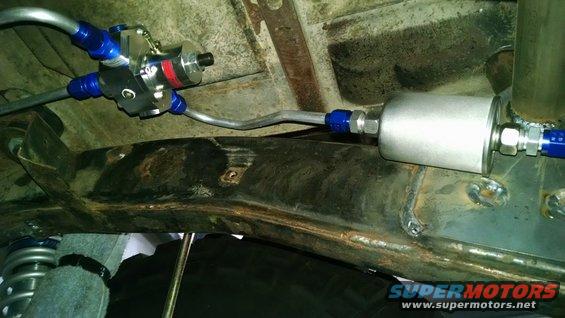 Underside view of a fuel filter and regulator assembly with blue fittings attached to rusty frame