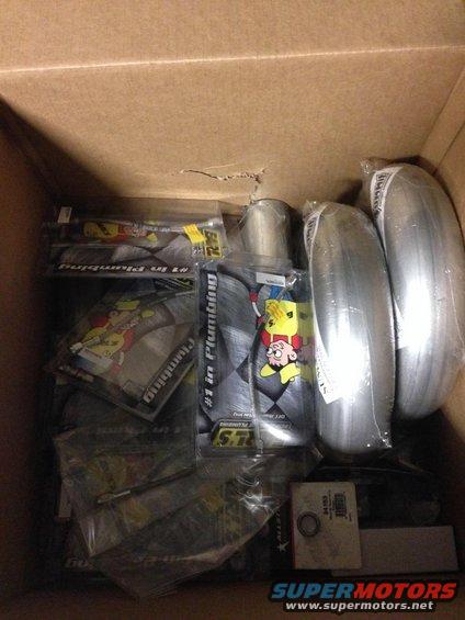 Box of assorted automotive parts including exhaust pipes and packaging with cartoon characters