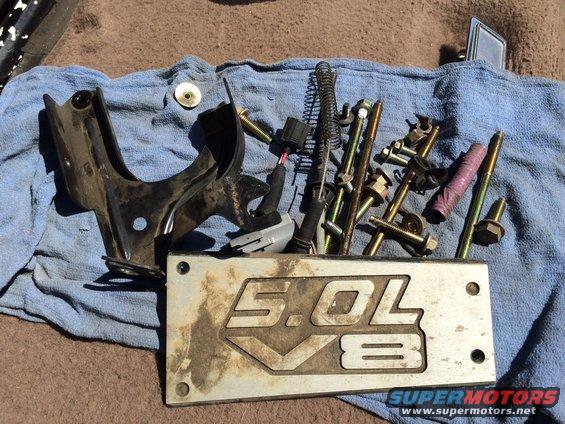 Metal plate with "5.0L V8" engraving and engine parts on a blue cloth