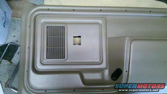 Tan interior door panel with speaker grille and square cutout for window crank
