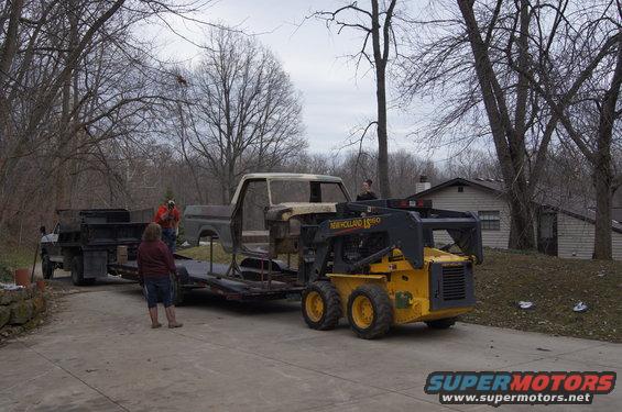 Ford F-Series truck cab on a trailer being loaded by a skid steer loader