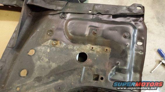 Rusty metal car part with bolt holes and a central circular opening