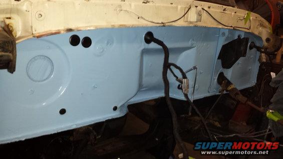 firewall area of a vehicle, painted light blue, with wiring harness visible