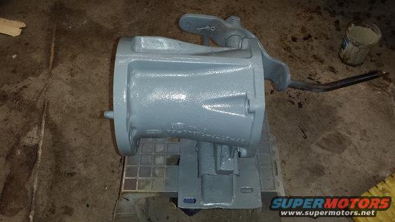 gray painted transmission housing with a lever attached, sitting on a stand