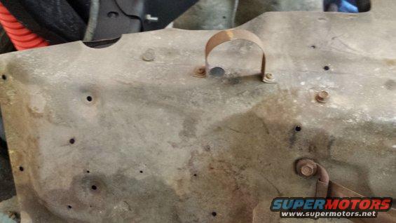 Rusty metal panel with holes and a U-shaped clamp, viewed up close
