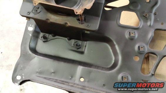Close-up of a black metal car part with mounting holes and brackets