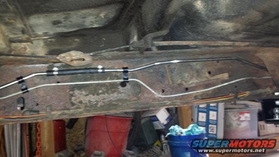 Undercarriage of a vehicle showing rusty frame and new brake lines, with red and blue buckets visible below