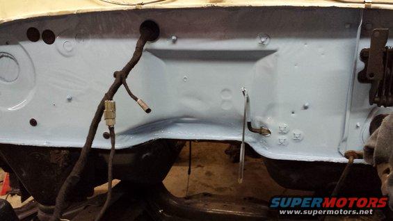 Light blue painted vehicle firewall with black wiring harness and metal brackets