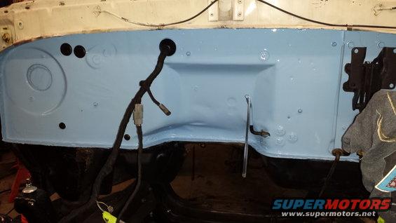 firewall area of a vehicle, painted light blue, with wiring harness