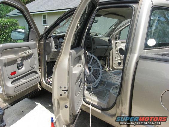 Interior of a pickup truck with doors open, fan on floor, and some panels removed