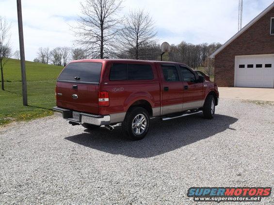 Red 2008 Ford F-150 pickup truck with a camper shell parked on a gravel driveway