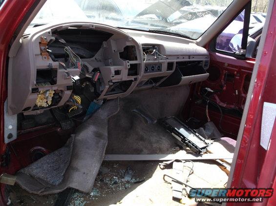 Interior of a red car with dashboard removed, wires exposed, and parts scattered on the floor