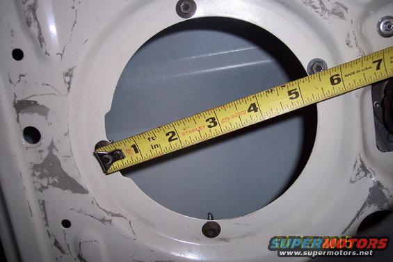 Measuring a circular cutout in a car door panel with a yellow tape measure