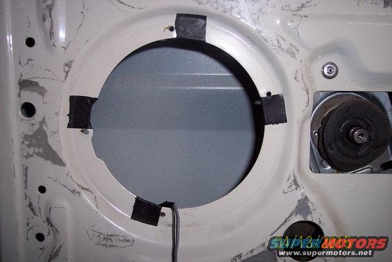 Interior door panel with speaker mounting hole and wiring. Part of a motor visible