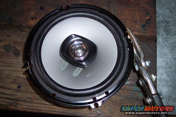 Car speaker with silver cone and black surround, held by vise grips