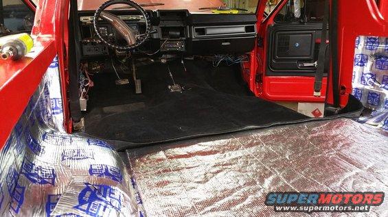 Red 1980s truck interior with black carpet and sound deadening material on the floor and door panels