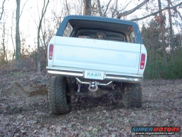 Rear view of a white Ford Bronco with a black top, parked on a muddy trail
