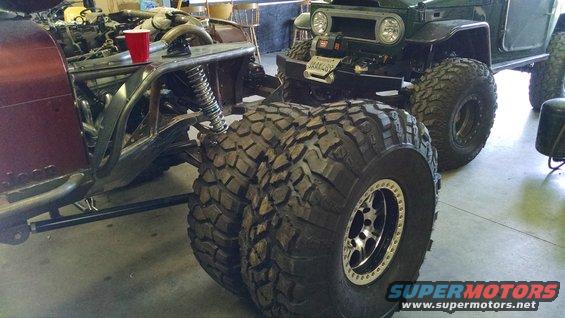 Maroon off-road vehicle chassis with exposed engine and large dual tires, next to a green vehicle