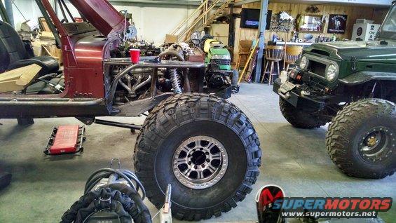 Maroon Jeep CJ-series with large off-road tires, undergoing customization